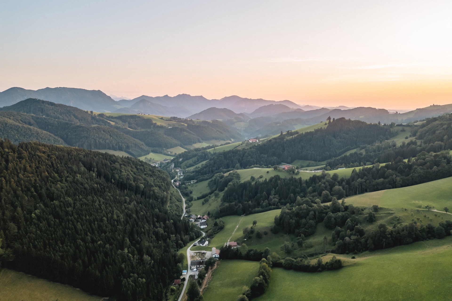 Luftaufnahme eines Voralpentals mit Wiesen, Wald und verstreuten Höfen im Abendlicht