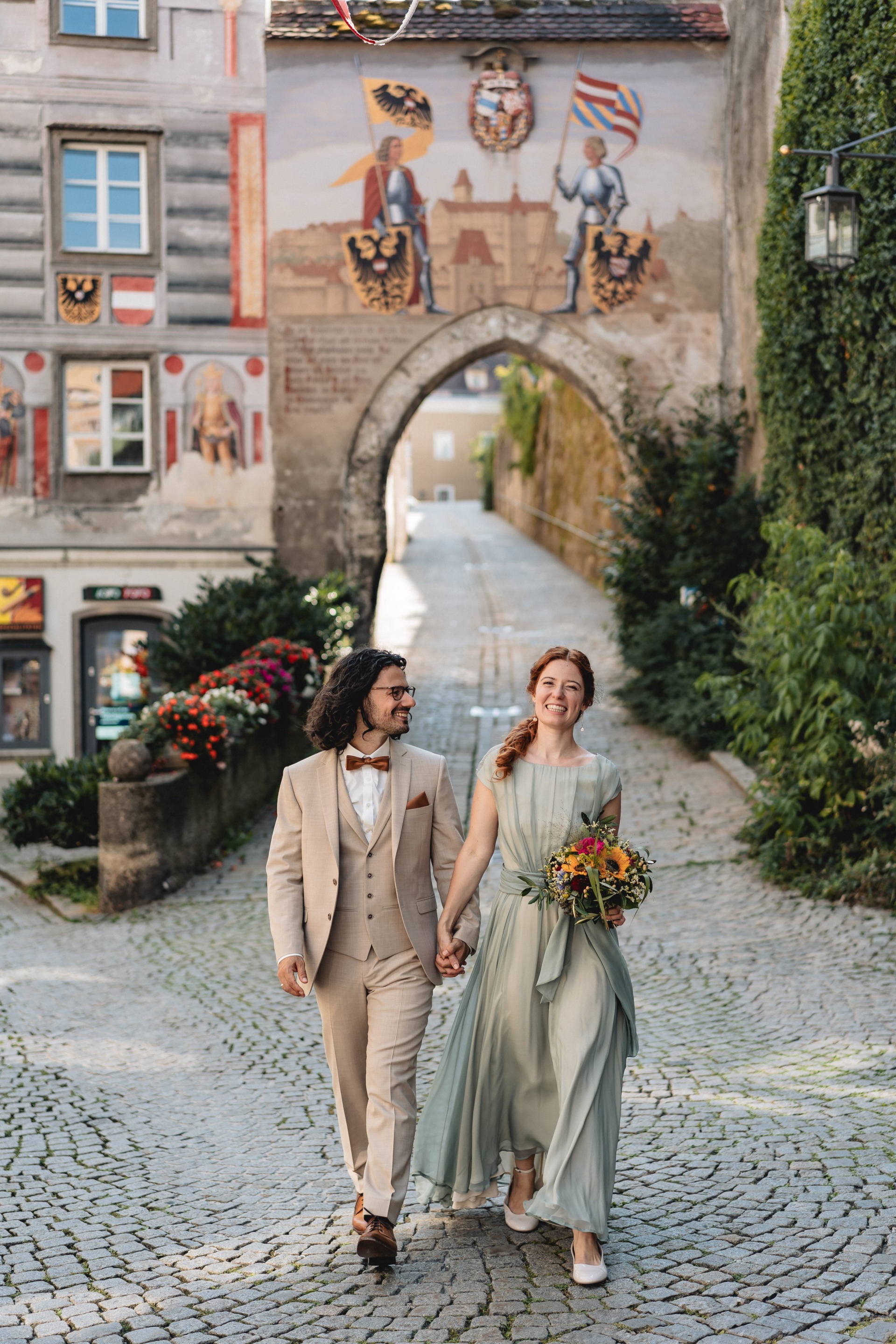Hannah und Alexis gehen Hand in Hand durch ein bemaltes Stadttor