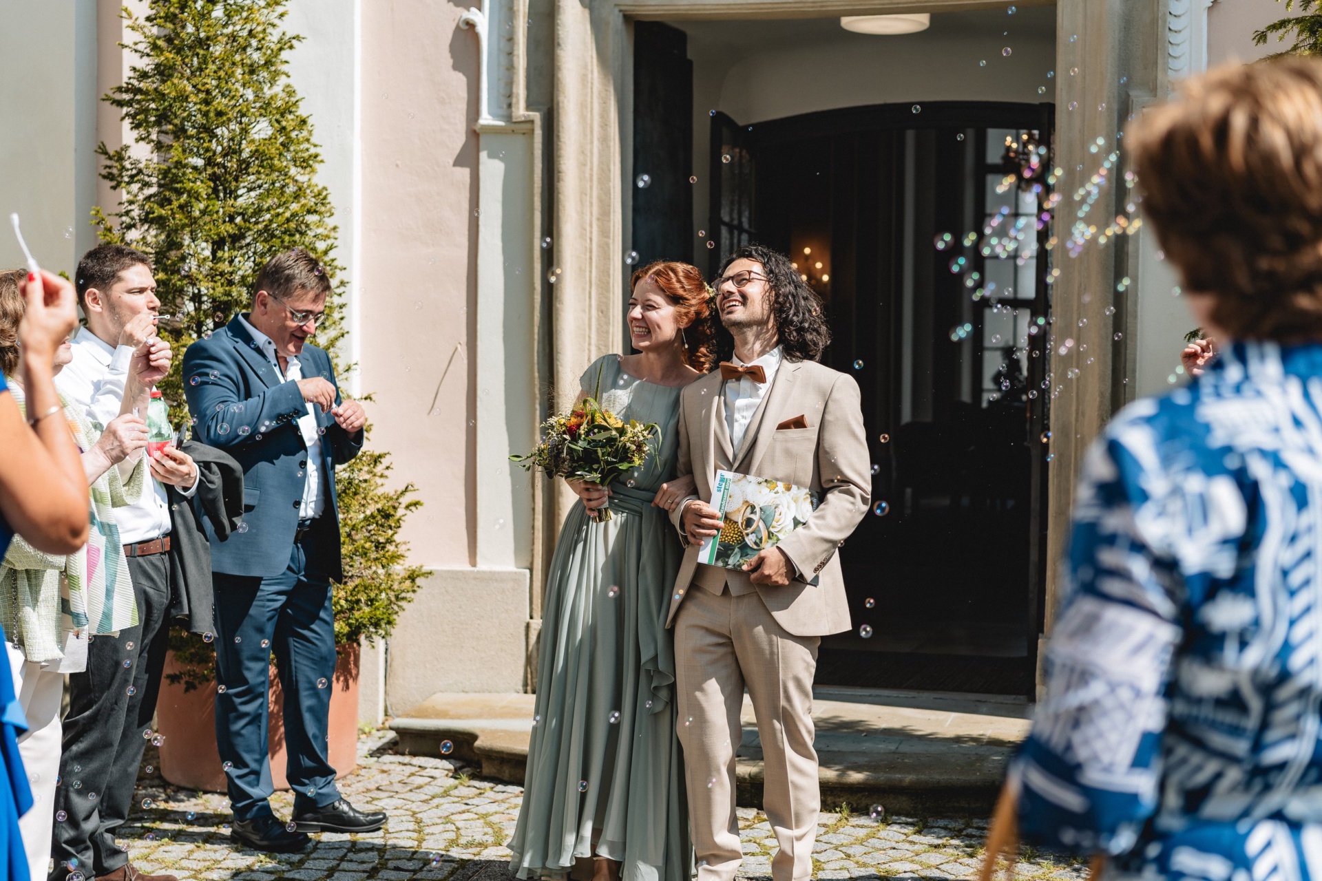 Hochzeitspaar tritt unter Seifenblasen aus dem Standesamt