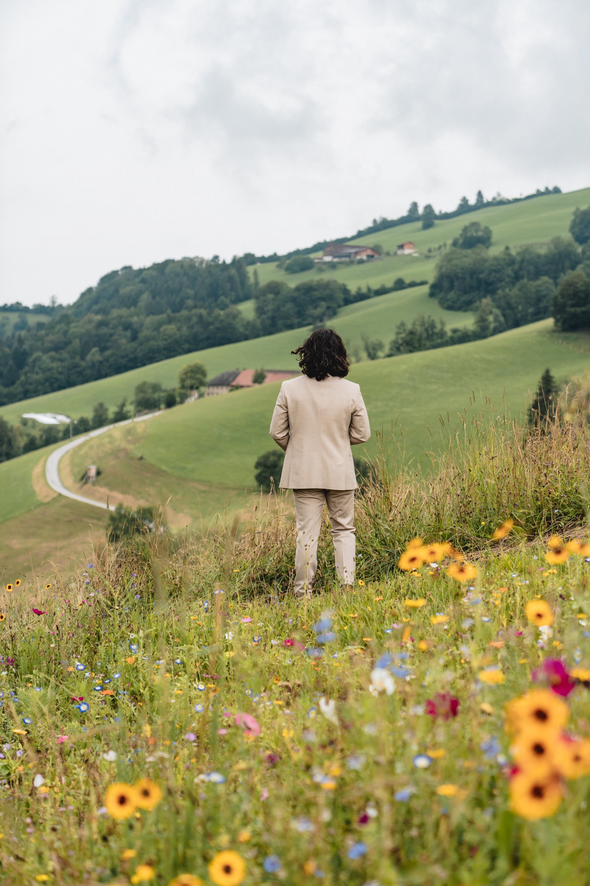 Alexis wartet mit dem Rücken zur Braut auf der Blumenwiese auf den First Look