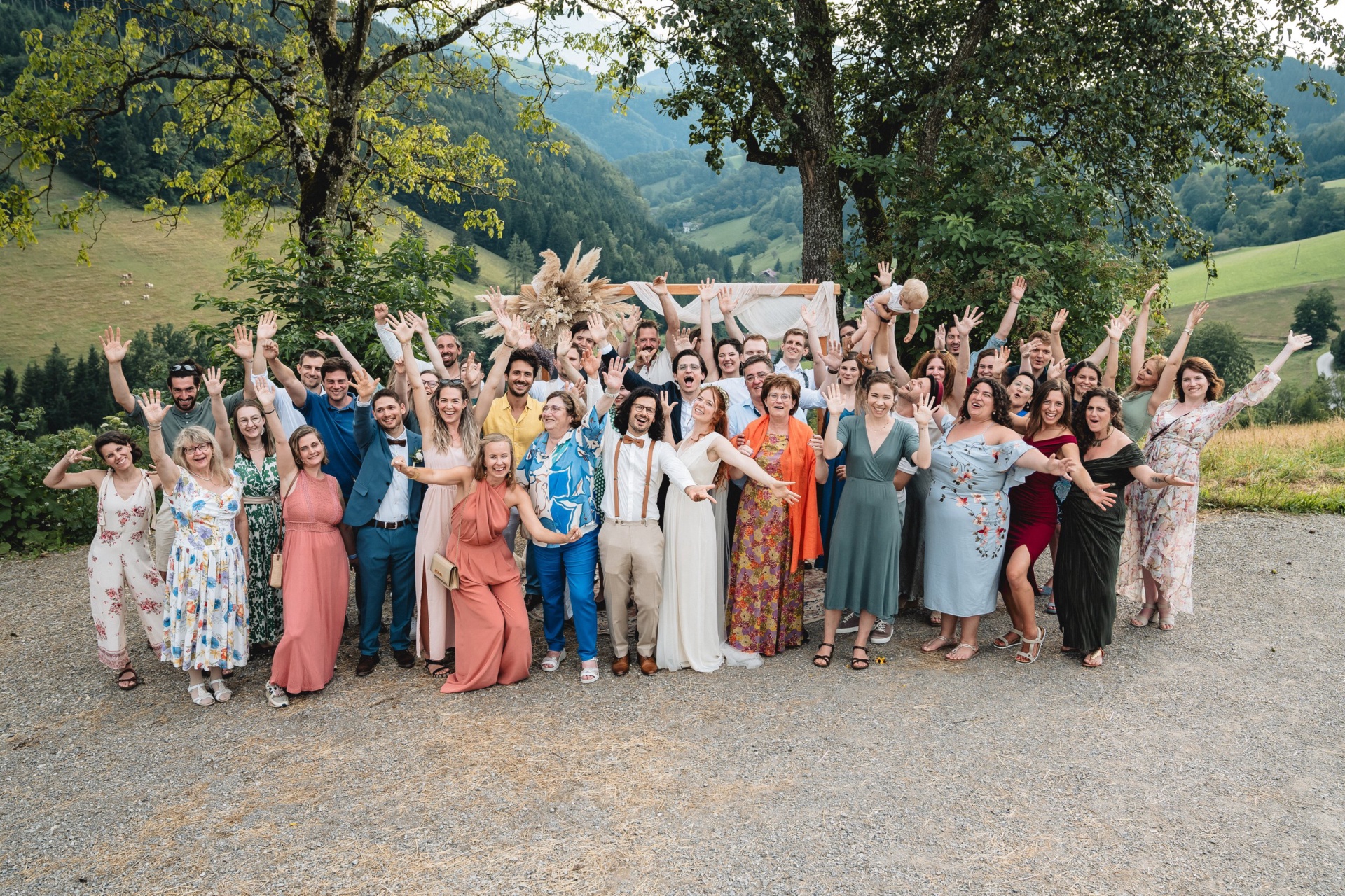 Gruppenfoto aller Hochzeitsgäste mit erhobenen Armen vor der Talkulisse